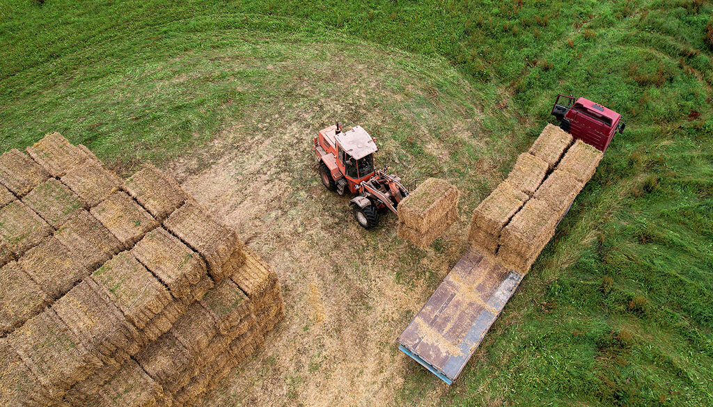 Aerial Shot of a Tractor Loading Square Hay Bales on a Flatbed Trailer in a Field Flatbed Trailers for Hay Hauling