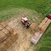 Aerial Shot of a Tractor Loading Square Hay Bales on a Flatbed Trailer in a Field Flatbed Trailers for Hay Hauling