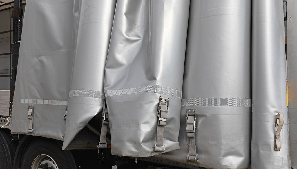 Closeup Of A Grey Tarp Hanging Over The Side Of A Trailer Tarp System Maintenance